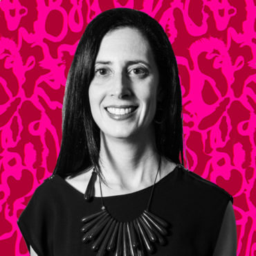 A black and white cutout photo of Shana Danon of Emilio Frank Design is superimposed over a bright pink and red abstract background. Shana has long dark hair and is wearing a short sleeved dark shirt and a necklace with a number of pendant beads arranged like the rays of the sun.