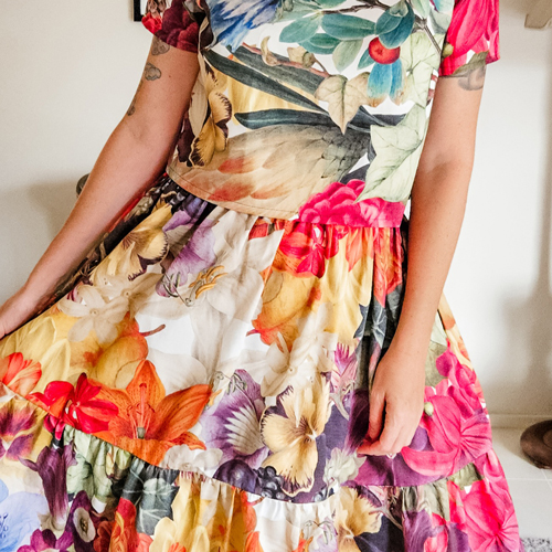 Kathryn Shaw of brand Rattamatatt wearing a floral custom print dress. She is holding the dress out to the side and the prink is by Anika Cook.