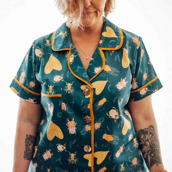 A closely cropped photo of a white woman with tattoos on her forarms. She is wearing a pyjama top that was made using custom printed fabric from the artwork library at Next State.