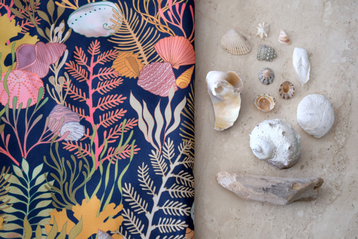 underwater inspired fabric on the sand with shells next to it