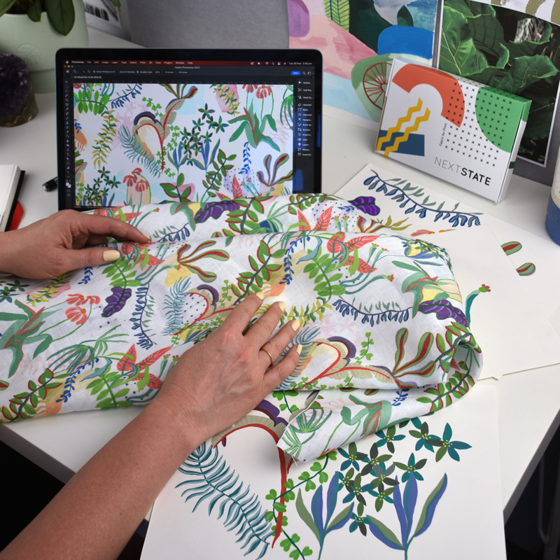 Fabric Printing New Zealand a girl is holding floral fabric in front of the same design on a computer screen that has been custom printed