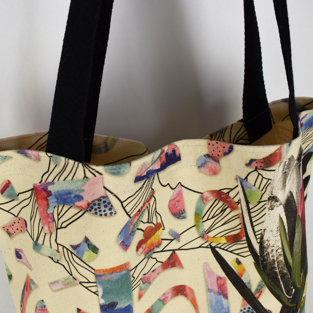 close up of a Next State custom print tote bag fabric and black straps. collaged bright artwork on the fabric.